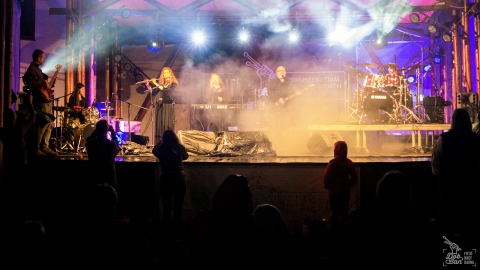 13. Dob-Ban Ritmusfesztivál - Santana dobosával zenélt a Role a csíki városnapokon - 13. Dob-Ban Ritmusfesztivál - Santana dobosával zenélt a Role a csíki városnapokon
Az esős idő és hideg ellenére hatalmasat dörrent a 13-ik Dob-Ban Ritmusfesztivál.
A városnapok színes program kínálata, az igencsak változatos tematikájú helyszínek közepette egy külön kis szigetnek számított a nemzetközi hírnévnek örvendő, hangulatos fesztivál.
Úgy a kimondottan igényes zenekedvelők, mint az egyszerűen csak szórakozni vágyók is olyan élmény-kavalkádban részesülhettek az idén augusztus 3-án, a csíkszeredai Mikó vár udvarán, amelyre büszke lehetne a világ bármely országának akármelyik nagyrendezvénye. Hol máshol játszik együtt magyar vers megzenésítéseket egy olyan amerikai világsztár, mint Jimmy Keegan a csíkszeredai Role zenekarral, miközben azt a közönség részeként, mint egy nagy család, együtt élvezik a helyi és messziről érkezett, világhírű zenészek.
Mert a csíki közönség a rendkívül kedvezőtlen időjárás ellenére kitartott, dacolva esővel, hideggel, széllel, és bizony megérte ott lenni egész nap! Már reggel 10-től bepillantást nyerhettek az érdeklődők a ritmus világába Cserey Csaba izgalmas dobkurzusa által, amelyet az egyik plakátfő: Jimmy Keegan káprázatos workshopja követett. Ritka élmény és páratlan lehetőség ily közelről megfigyelni, érezni egy kivételes tudású zenész óriási dinamikájú, energikus játékát, ellesni apró trükkjeit és élvezni kedves, közvetlen, színes személyiségét.
Majd jöttek az olyan lehetőségek úgy a gyerekek, mint a felnőttek számára, mint: a henna testfestés, hangszersimogató és kiállítás, hangszerkészítés, vagy Csabcsi zenés mesejátéka a király udvari dobosáról, akinek végigkövethettük ritmusokkal és humorral teli útját. Mindeközben a szakadó esőben zajlottak az esti koncertek hangpróbái, lépten-nyomon összetalálkozhattunk a készülődő, feszülten koncentráló, ám kedvesen mosolygó világsztárokkal.
A koncertek:
A fesztivál rendkívül gazdag koncertprogramja hónapokra feltöltötte még a legvájtabb fülű érdeklődők lelkét is a lehető legszínesebb, magas színvonalú zenei élményekkel. Hiszen itt nem csak órákig tartó dobolásról volt szó, hanem a zenéről magáról. Külön kiemelendő az a tény, hogy a világsztárok mellett helyet kaptak feltörekvő helyi tehetségeknek is: a csíkszeredai diákokból álló The Morning After minikoncertjét élmény volt hallgatni. Tehetségük, a zenéhez való pozitív, alázatos hozzáállásuk nagy jövőt ígér.
A Blues and Drums a már fentebb említett gyergyói/csíki származású Cserey Csaba és a szatmári Vékony Joe József gitáros, énekes duója. Igazi, vérbeli blues hangulatot hoztak a színpadra, amelyben hazai “veteránjaink” igazán otthonosan mozogtak.
A harmadik koncert során két ifjú ütőhangszeres izgalmas zenés újratalálkozásának lehettünk tanúi: Szabó Csongor-Zsolt és Székely Voland 10 év után játsztak újra együtt a színpadon SzX2 néven. Élmény volt hallgatni profi, érett produkciójukat, amelyben az Ausztriában élő, ott perkúciózó Voland régi ismerősként tért vissza Dob-Ban-ra.
És akkor jött a temesvári JazzyBIT koncertje. Sziporkázó, játékos, szórakoztató, jazzes, fusionos zenéjüket, laza, könnyedd, fiatalos előadásmódjukat lehetetlen volt mosolygós bulizás nélkül kibírni. Szellemes, ötletes, friss megoldásokkal telített zenéjük igazi élményt jelentett mindenkinek.
A következő fellépőről, a norvég 27 éves Baard Kolstadról sokan csak a beharangozókban elhangzott infót tudták, miszerint a progresszív zene új “fenegyereke”, de az utóbbi években nagyon sokan hallhatták őt a világ legnagyobb fesztiváljainak színpadjain zenekarával, a Leprous-szal. Bár kissé türelmetlenné tette közönségét a dobfelszerelése hosszas beállításával, de aztán másodpercek alatt meghódította a hallgatóság szívét-lelkét káprázatosan energikus, rendkívül technikás előadásmódjával, bebizonyítván, hogy nem véletlenül tartják az új dobosgeneráció egyik legjobbjának.
A norvég energiabomba dobos show-ja után majdnem biztosak voltunk benne, hogy ezt már nem lehet fölülmúlni... márpedig lehetett: törékeny, leheletfinom, éteri dallamokkal, misztikusan lüktető ritmusokkal. A hihetetlenül szép, keleti fúvós- és énekdallamok varázslója, az iráni Mehdi Aminian és a világszerte közkedvelt, szibériai Nadishana perkúciós, hangszerfeltaláló zseni duója már csak azért is sikeredett rendkívülire, mert e két zenei nagyság Csíkszeredában, a ritmusfesztivált megelőző napokban találkozott első ízben. A hideg észak találkozott a meleg kelettel, életükben először és ez a találkozás egy olyan gyönyörű koncertet hívott életre, amely szárnyakat adott képzeletünknek, kirángatva a hallgatóságot az est hidegének és az újabb felhőszakadásnak nyomasztó hangulatából.
...és jött a fesztivál utolsó koncertje: a világsztár, Jimmy Keegan ismét kitörölhetetlenül belopta magát a Dob-Ban ritmusfesztivál közönségének szívébe, hiszen szakmai tudása, rendkívüli tehetsége, muzikalitása, és mérhetetlen kedvessége, nemes egyszerűsége ismét rádöbbentett mindnyájunkat arra, hogy az igazi nagyság nem szorul semmilyen celebkedésre. Gyönyörű koncertnek, fergeteges dobszolóknak lehettünk tanúi, amelyet megtetézett a végén azzal, hogy a fesztiválszervező csapat gerincét alkotó Role zenekar tagjait felhívta a színpadra, együtt játszva velük Ady Endre és József Attila verseire írt dalaikat.
Amit megtapasztalhattunk az idei, a 13-ik Dob-Ban Ritmusfesztiválon is, az maga a páratlan közösségi élmény, amelyben együtt, közösen hozzák létre a varázslatot: a nagyszerű előadók, a nagyon fiatal, lelkes önkéntes csapat, a „válogatott” technikai stáb, az esővel, hideggel dacoló lelkes és odaadó közönség, a minden előreláthatatlan akadállyal „is” keményen megküzdő szervezőcsapat. Olyan közvetlen, családias hangulatot sikerült létrehozni e csodás helyszínen, a Mikó-vár-ban, így együtt a partnerekkel, támogatókkal, ami valószínűleg ritkán, vagy egyáltalán nem jellemző az ilyen kaliberű művészeket felvonultató rangos rendezvényekre sehol e világon.
A csíkszeredai Agora Alapítvány köszönetét fejezi ki Csíkszereda Polgármesteri Hivatalának, Hargita Megye Tanácsának, a Hargita Megyei Kulturális Központnak és Magyarország Csíkszeredai Főkonzulátusának, a XIII. DOB-BAN Ritmusfesztivál megvalósításához nyújtott támogatásáért, és a csodás közönségnek a kitartásáért!
